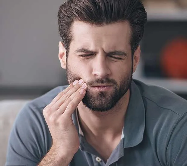 man touches face in pain