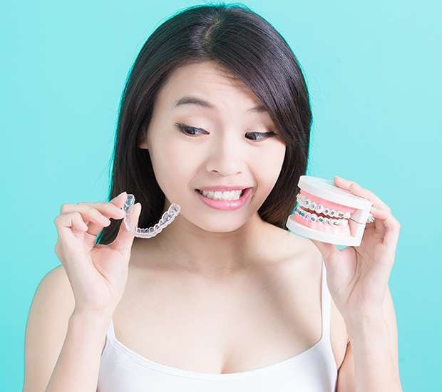 woman holds invisalign tray and braces model