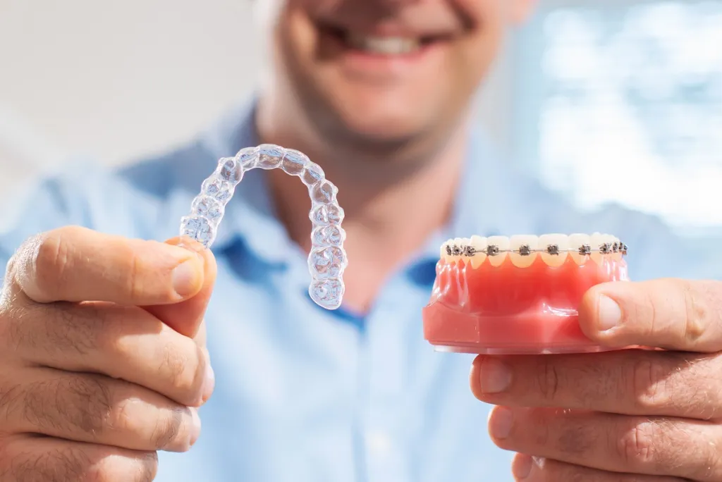 man holds clear aligner and braces model